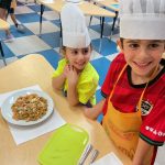 Kids in chef hats with pasta dish.